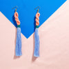 Light Pink knot and blue tassel earrings in front of blue + pink background